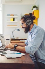 Praktische Gadgets fürs Homeoffice Eine Person sitzt vor einem Laptop an einem Schreibtisch und trägt ein Headset.