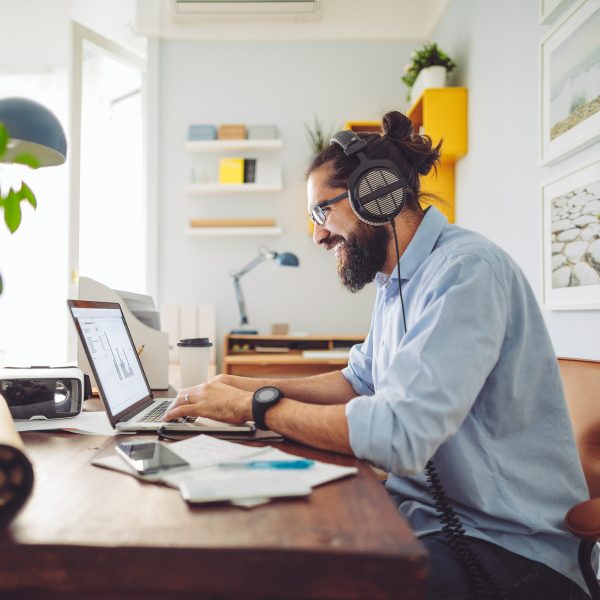Eine Person sitzt vor einem Laptop an einem Schreibtisch und tr&auml;gt ein Headset.