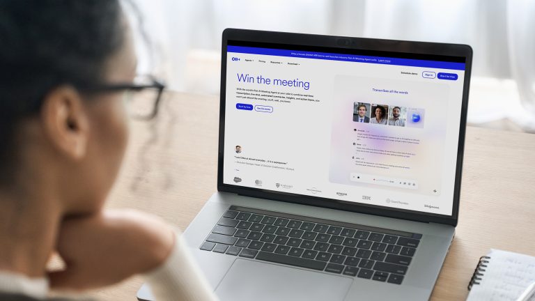 KI App, Mach dir deinen Alltag einfach mit diesen Apps Ein geöffneter Laptop steht auf einem Holzschreibtisch. Auf dem Display ist die На главную von Otter.ai zu sehen. Eine Person sitzt vor dem Laptop.