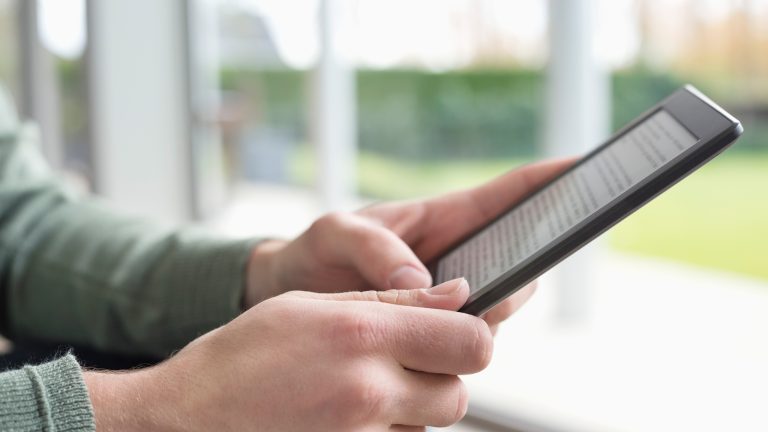 Kindle Unlimited, So kündigst du das E-Book-Abo Nahaufnahme zweier Hände, die ein Tablet halten. Das Display zeigt einen Fließtext.