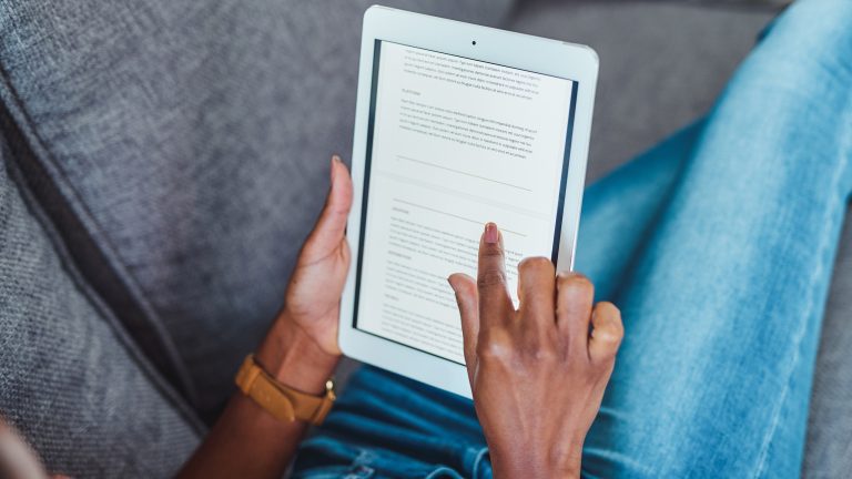 Kindle Unlimited, So kündigst du das E-Book-Abo Auf dem Display eines Tablets ist ein Fließtext zu sehen. Eine Person, in einer bequemen Liegeposition hält das Tablet in den Händen. Das Gesicht ist nicht zu sehen.