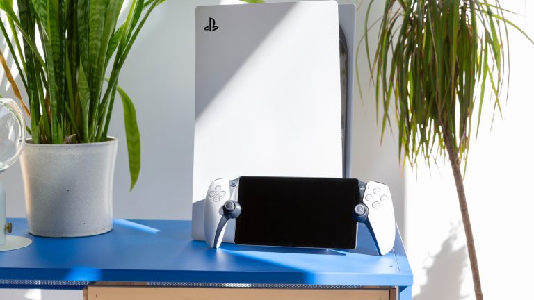 Ein PlayStation Portal steht in der Sonne angelehnt an eine PlayStation 5 auf einem Sideboard. Rechts und links daneben sind Pflanzen.