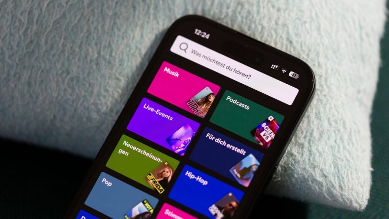 Podcast Apps, Diese Apps gibt es Eine Nahaufnahme eines iPhones, das an einem Kissen lehnt. Darauf ist die Auswahlseite der App Spotify zu sehen.
