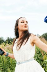 Eine Person steht auf einer Wiese. In einer Hand hält sie einen Bluetooth-Lautsprecher, in der anderen Hand ein Smartphone.