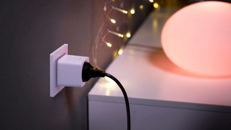 Erstaunlich nützliche Technik-Gadgets für unter 100 Euro Nahaufnahme einer smarten Steckdose mit einem schwarzen Stecker. Im Hintergrund ist ein Lowboard mit Kugellampe zu erkennen.
