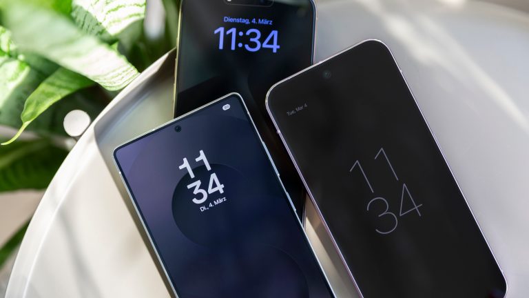 iPhone 16 Pro Max vs. Galaxy S25 Ultra vs. Google Pixel 9 Pro XL, Premium-Smartphones im Vergleich Ein iPhone 16 Pro Max, ein Galaxy S25 Ultra und ein Pixel 9 Pro Max mit eingeschalteten Always-on-Displays auf einem Tisch.
