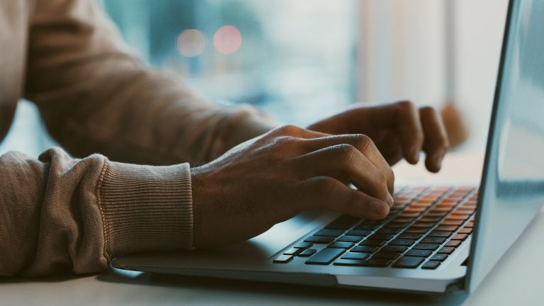 Wasserzeichen in Word einfügen und bearbeiten Seitenansicht eines geöffneten Notebooks. Die Hände einer Person liegen auf der Tastatur.