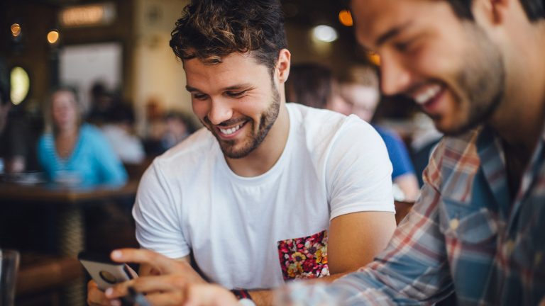 Was ist TikTok? Übersicht und erste Schritte Zwei Personen sitzen an einem Tisch, schauen etwas auf ihren Smartphones und lächeln dabei.