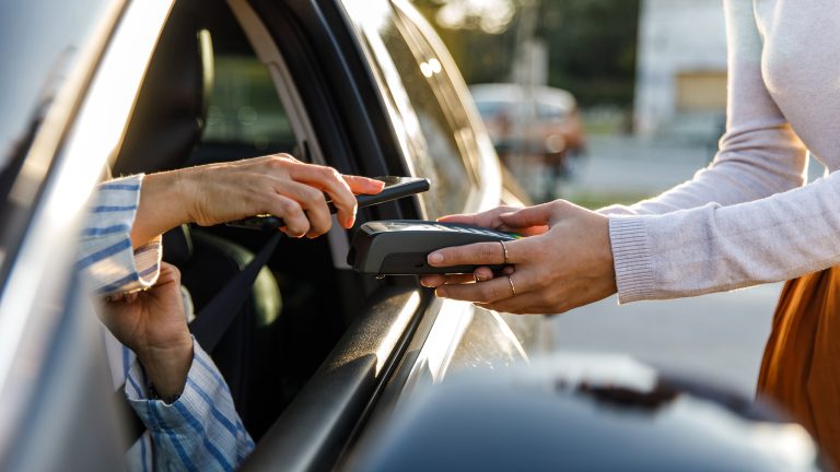 Apple Pay, Bezahlen mit iPhone, iPad und Apple Watch Eine Person hält ihr Smartphone aus dem Fenster eines Autos auf ein Kartenlesegerät.