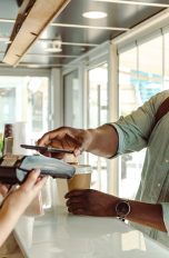 Eine Person hält ihr Smartphone an das Kartenlesegerät in einem Café.