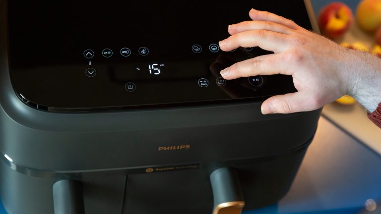 Frittieren ohne Fett, Funktionen einer Heißluftfritteuse Nahaufnahme des Bedienfelds einer Philips Heißluftfritteuse. Eine Hand drückt einen der Knöpfe.