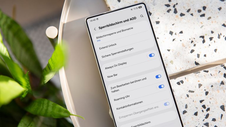 Ein Samsung Galaxy S25 Ultra liegt auf einem Tisch mit gesprenkelten Unterlagen, daneben die Blätter einer Pflanze. Auf dem Screen sieht man die Einstellungen zum Sperrbildschirm und AOD.