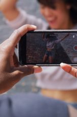 Eine Person im Anschnitt filmt mit dem Smartphone in beiden Händen eine zweite Person beim Tanzen.