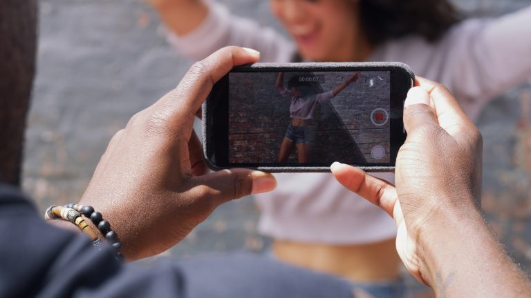 Eine Person im Anschnitt filmt mit dem Smartphone in beiden Händen eine zweite Person beim Tanzen.