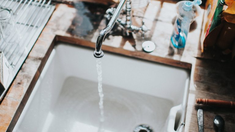 Wasserverbrauch Spülmaschine, Hand vs. Maschine Blick in ein Spülbecken. Der Wasserhahn läuft.