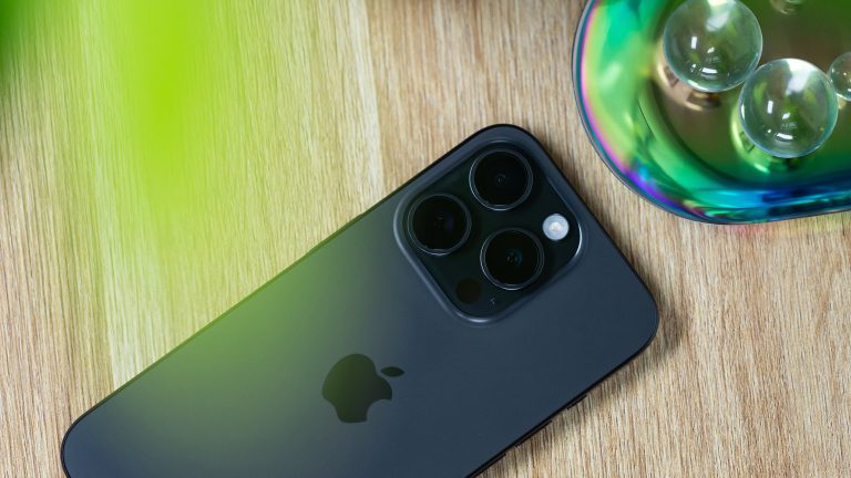 iPhone 15 Pro & Pro Max, Noch immer sehr interessant Blick auf ein iPhone 15 Pro, das mit der Rückseite nach oben auf einer Holzoberfläche liegt.