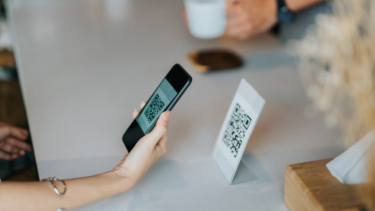 QR-Code erstellen, Mit diesen Apps und Services klappt es Eine Person hält ein Smartphone mit aktivierter Kamera an einen ausgestellten QR-Code.