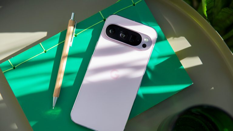 Das Google Pixel 9 Pro in rosa liegt auf einem Tisch auf einem grünen Notizbuch. Daneben ein Stift.