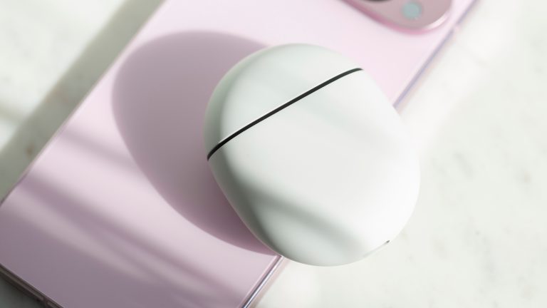 Das weiße Ladecase der Pixel Buds Pro liegt auf einem rosafarbenen Pixel 9 Pro.