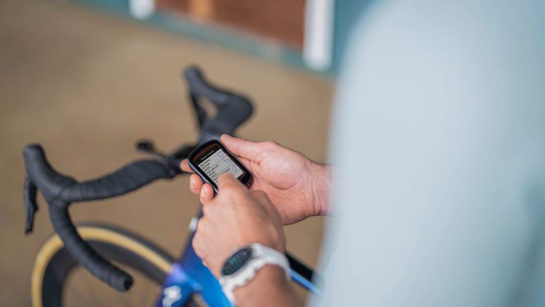 Garmin Connect synchronisiert nicht, Probleme & Lösungen Eine Person hält einen Fahrradcomputer in den Händen. Im Hintergrund ist ein Gravelbike zu sehen.