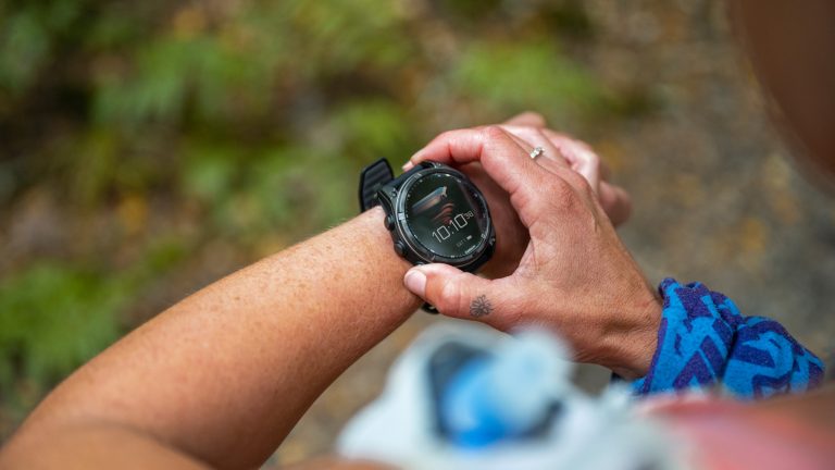 Garmin Connect synchronisiert nicht, Probleme & Lösungen Blick über die Schulter einer Person: Am linken Handgelenk trägt die Person eine Smartwatch. Mit der anderen Hand drückt sie die Knöpfe der Smartwatch.