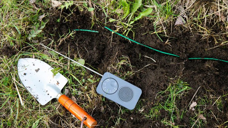 Mähroboter-Begrenzungskabel verlängern, So funktioniert’s Ein kleiner Stechspaten und ein Begrenzungskabeltester liegen im Gras.