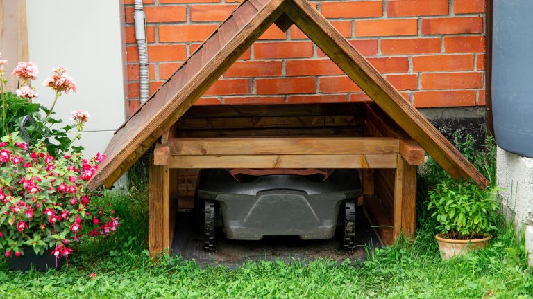Mähroboter-Zubehör, Garage, Ersatzteile & smarte Erweiterungen Ein Mähroboter steht in einer selbstgebauten Mähroboter-Garage aus Holz.