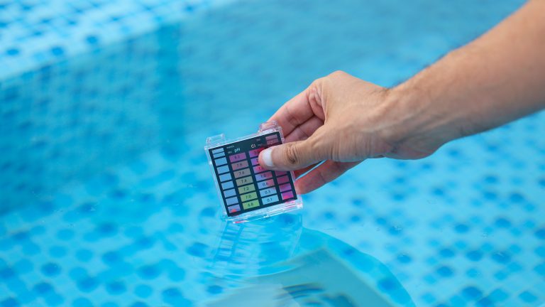 Poolroboter reparieren, So machst du’s selbst Eine Person hält eine Karte zum Testen des PH-Werts in das Wasser eines Pools.