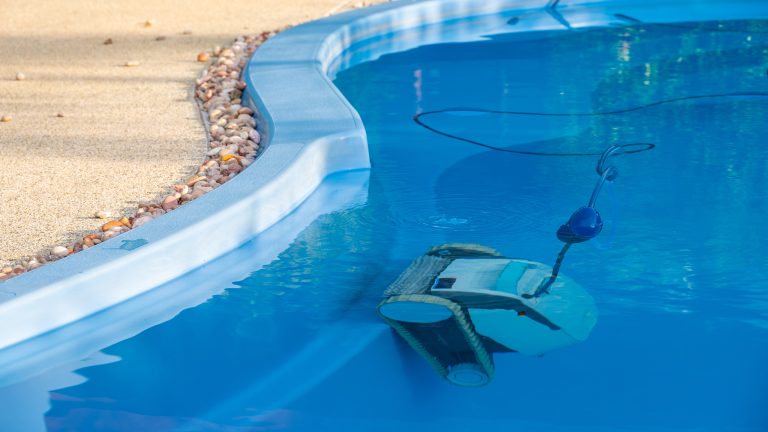 Poolroboter reparieren, So machst du’s selbst Blick auf die Seite eines Pools in dem ein Poolroboter senkrecht an einer Kante steht.
