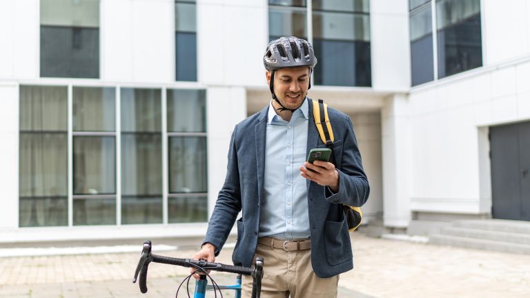 Smarte Helme, Was du darüber wissen musst Eine Person mit einem Fahrrad und einem Helm auf dem Kopf schaut auf ihr Smartphone.