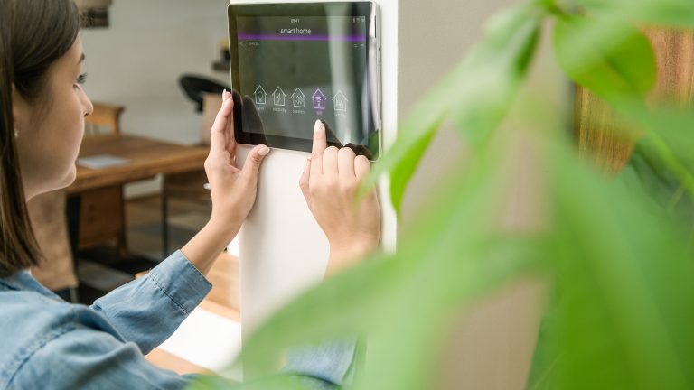 Eine Person steuert Smarthome-Funktionen &uuml;ber ein an der Wand montiertes Tablet.