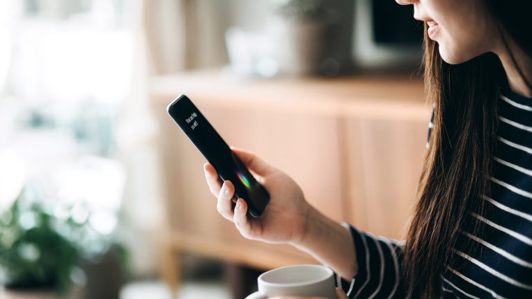 Eine Person h&auml;lt ein Smartphone in der Hand, auf dem ein Sprachassistent zu sehen ist.