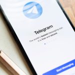 Ein Smartphone auf einem Schreibblock. Links daneben ein Kugelschreiber. Auf dem Screen der Startbildschirm von Telegram.