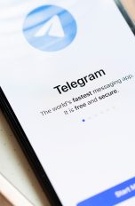 Ein Smartphone auf einem Schreibblock. Links daneben ein Kugelschreiber. Auf dem Screen der Startbildschirm von Telegram.