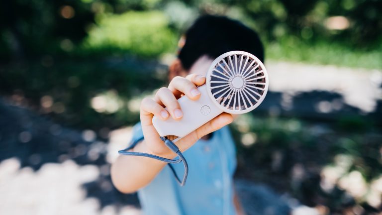 Praktische Balkon-Gadgets für Frühling und Sommer Im Fokus steht die Rückansicht eines mobilen Mini-Ventilators, den eine Person in blauem Shirt in den Händen hält.