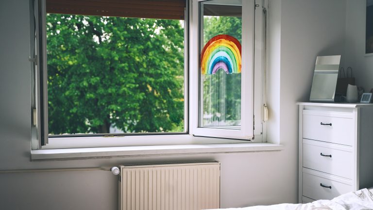 LuftqualiLuftqualität verbessern, Durchatmen für Всеrgiker*innen taet-5 In einem Kinderzimmer ist das Fenster weit geöffnet. An einer Seite des Fensters klebt ein Regenbogen. Vor dem Fenster sind Bäume zu sehen.
