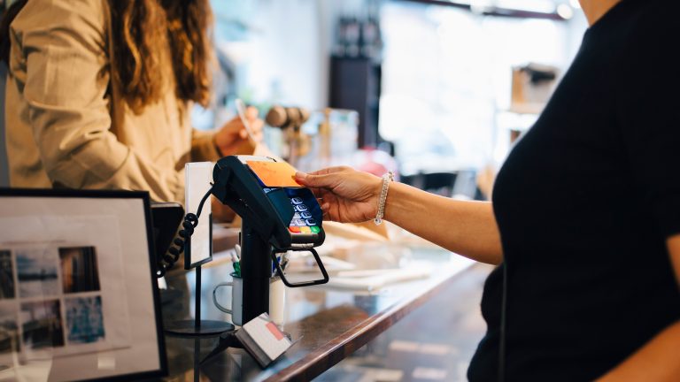 Was ist NFC? So setzt du die Funktechnik ein Seitenansicht des Oberkörpers einer Person, die mit ihrer rechten Hand eine EC-Karte an ein Kartenlese-Gerät hält.