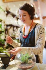 Eine Person steht in einem Blumenladen an der Kasse. Sie hält ihr Smartphone ans Lesegerät, um zu bezahlen.