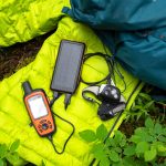 Ein Satellitenkommunikationsgerät liegt auf einem neongrünen Schlafsack. Daneben liegt ein dunkelblauer Outdoor-Rucksack.