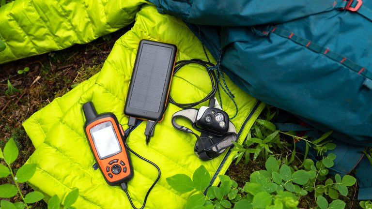 Ein Satellitenkommunikationsgerät liegt auf einem neongrünen Schlafsack. Daneben liegt ein dunkelblauer Outdoor-Rucksack.