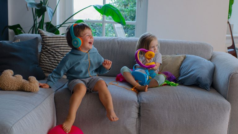 Zwei Kinder auf einem Sofa hören zusammen an einer Tigerbox MINI mit den Kopfhörern Tigerbuddies etwas.
