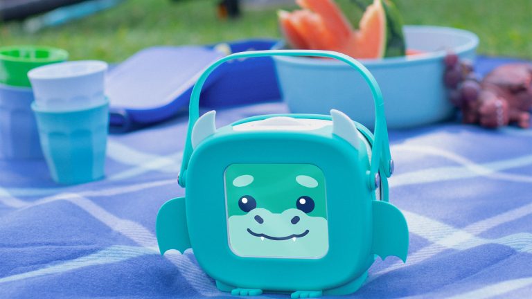 Tigerbox Mini, Süße Musikboxen kommen im September Eine Tigerbox Mini mit Drachen-Hülle steht auf einer Picknickdecke im Freien.