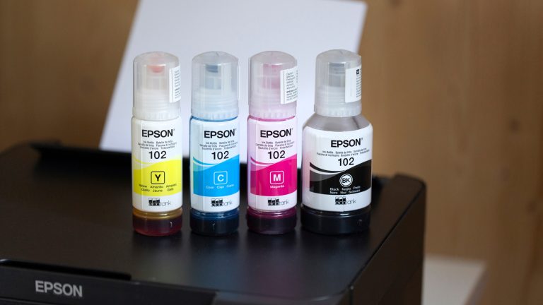 Epson Ecotank, Das können die verschiedenen Modelle Epson Tintenflaschen in Gelb, Cyan, Magenta und Schwarz stehen auf einem Epson EcoTank Drucker.