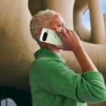 Eine Person steht vor einem futuristischen Gebäude und hält ein mintgrünes Google Pixel 10 Pro an ihr Ohr.
