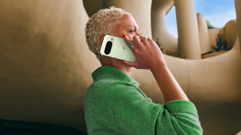 Google Pixel 10-Serie, Smarte Evolution mit Pixel Snap als Highlight Eine Person steht vor einem futuristischen Gebäude und hält ein mintgrünes Google Pixel 10 Pro an ihr Ohr.