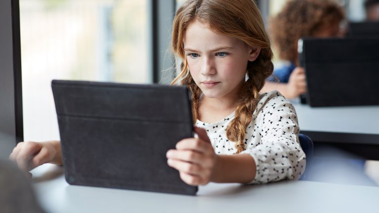 Tablets für die Schule, Diese Modelle eignen sich Ein Kind sitzt an einem Tisch an einem Fenster und schaut auf ein Tablet.