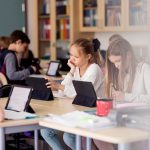Kinder in einer Schule sitzen an Tischen und bedienen Tablets vor ihnen.