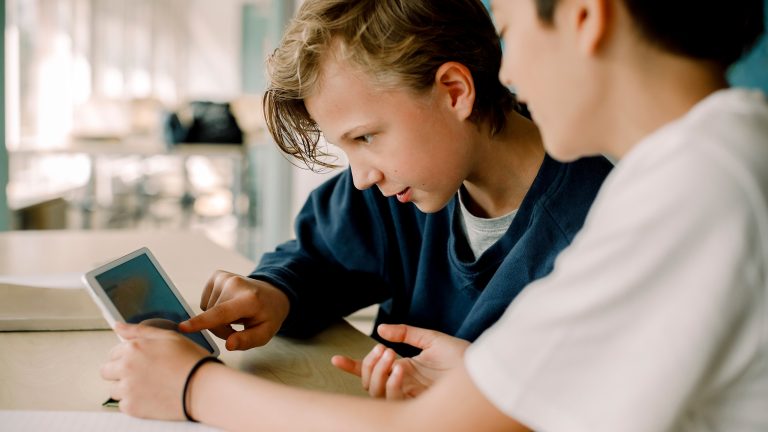 Tablets für die Schule, Diese Modelle eignen sich Zwei Kinder sitzen vor einem iPad Mini und schauen darauf etwas an.
