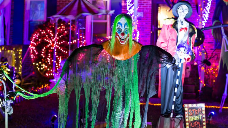 Ein schauriger Clown steht vor einem gruselig geschmückten Haus. Im Hintergrund ist eine weitere schaurige Figur zu sehen.