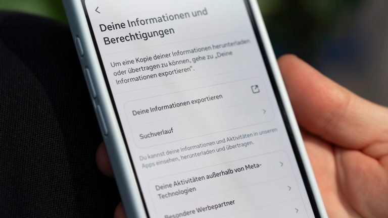 Instagram löschen oder deaktivieren, So entfernst oder pausierst du dein Konto Eine Nahaufnahme eines Smartphones in der Hand einer Person. Darauf die Einstellungsübersicht “Deine Informationen und Berechtigung” von Instagram.